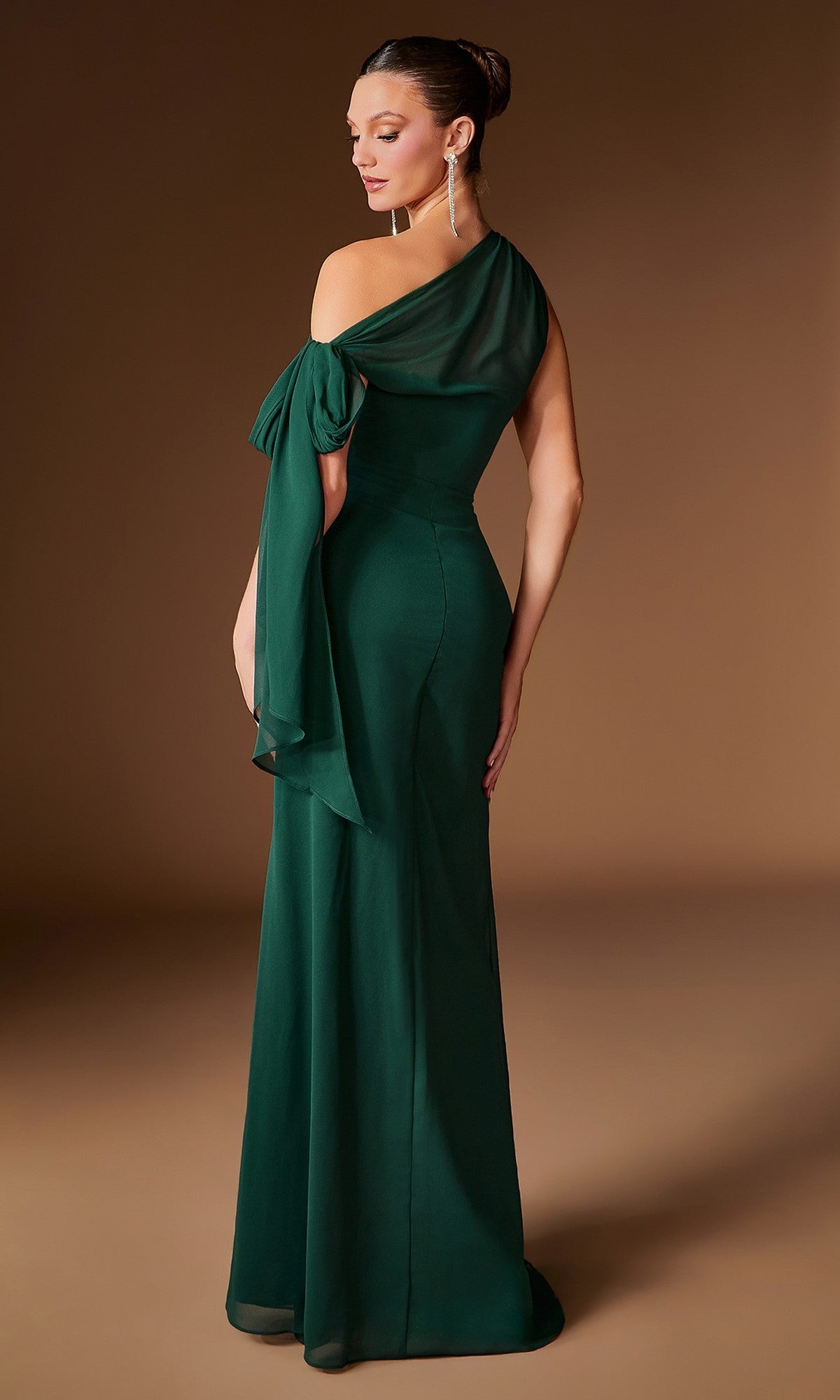 A woman stands facing away against a neutral background, wearing the Ladivine CH2612—a floor-length, dark green formal dress featuring a one-shoulder design, asymmetrical neckline, and bow detail.